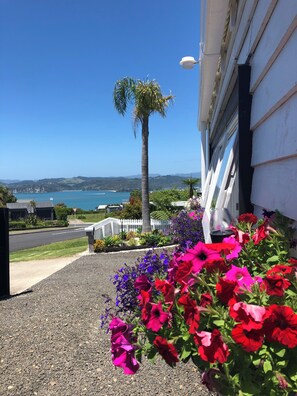 Una casa con camino de grava, flores vibrantes y vistas al mar y a las colinas.