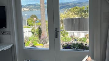 A room with a door leading to a balcony with a view of a lake and hills.