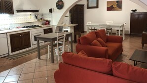 A kitchen with white cabinets, a dining table, and a red sofa. - Vacation House Zagara - Giardinello (Giardinello)