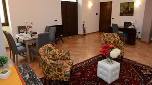 A living room with a dining area, floral armchairs, a white ottoman with flowers, a desk with a computer, and a painting on the wall. - Vacation House Zagara - Giardinello (Giardinello)