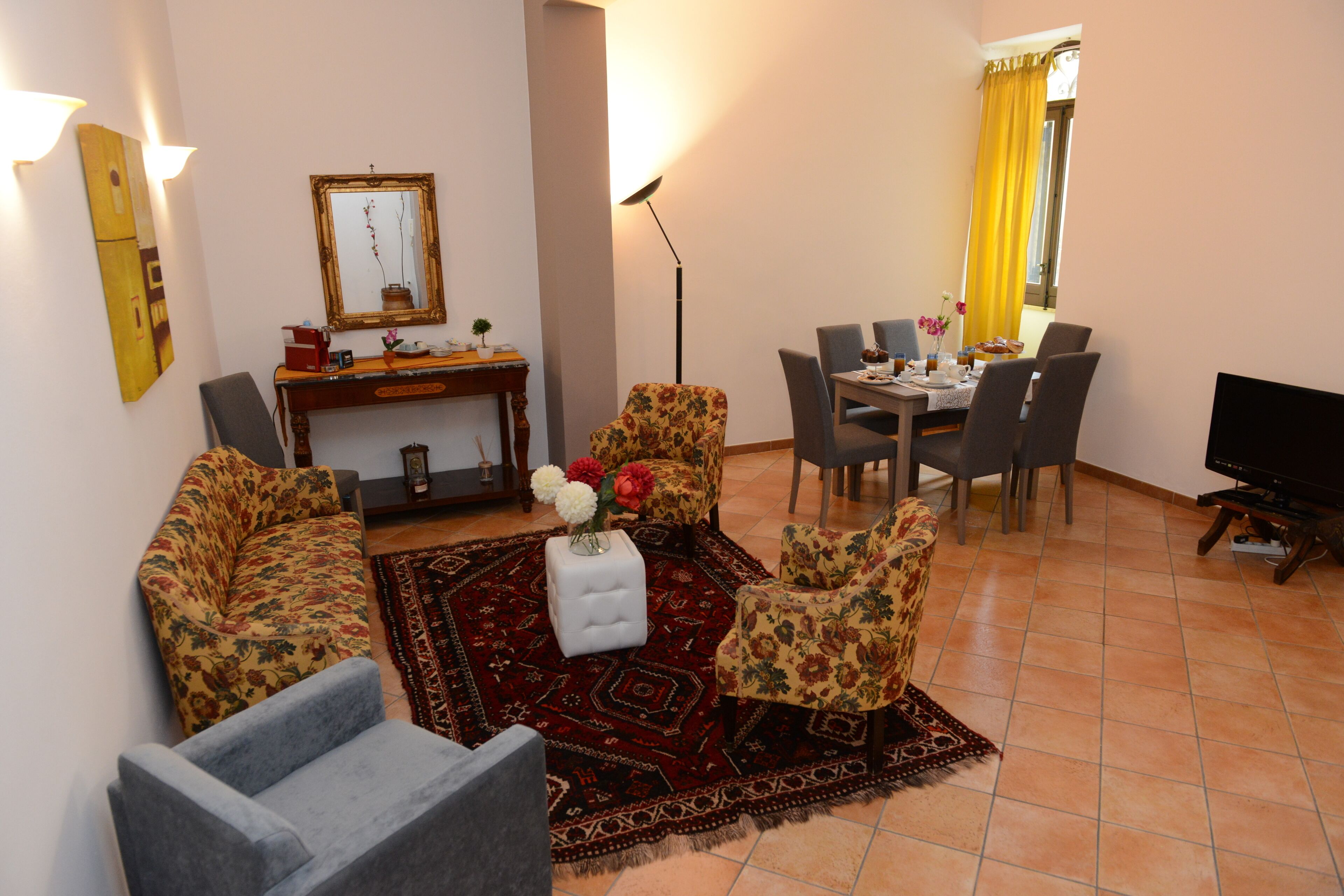 A living room with a sofa, armchairs, a coffee table, a dining table with chairs, a TV, and a floor lamp.