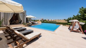 Area piscina con lettini, una sedia a dondolo e ombrelloni.