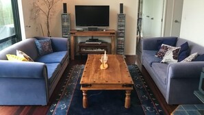 A living room with two sofas, a coffee table, a TV on a wooden stand, and a decorative tree. - Peaceful Ocean facing Island Escape (Kawau Island)