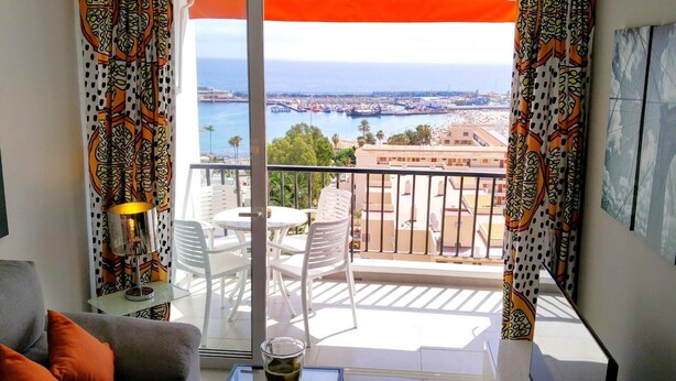 A balcony with a view of the sea and buildings, white furniture, and patterned curtains. - 5 minutes from the beach :Apartment Orange Trees panoramic ocean view (Los Cristianos)