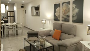 A modern living room with a grey sofa, a glass coffee table, and a dining area with a white table and chairs. - 5 minutes from the beach :Apartment Orange Trees panoramic ocean view (Los Cristianos)