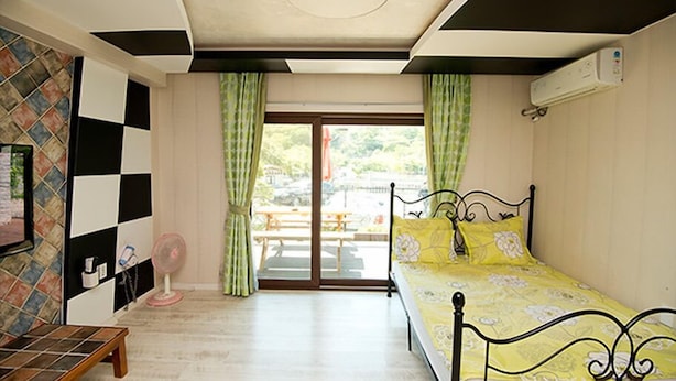 A bedroom with a bed, a small table, a fan, and a view of a patio with a table and chairs. - Ulsan Edelweiss Pension (Ulsan)