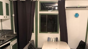 A compact kitchenette with a sink, stove, and storage cabinets. There is a window with curtains, a small table, and a bench with cushions.
