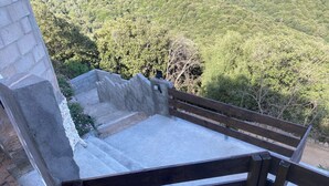 A stone bench with a metal frame, set against a backdrop of a stone wall and a lush green forest.