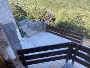 A stone bench with a metal frame, set against a backdrop of a stone wall and a lush green forest.