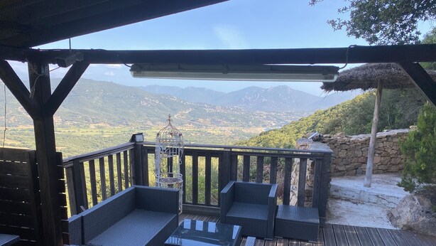 A wooden deck with wicker furniture and a birdcage, overlooking a mountainous landscape.
