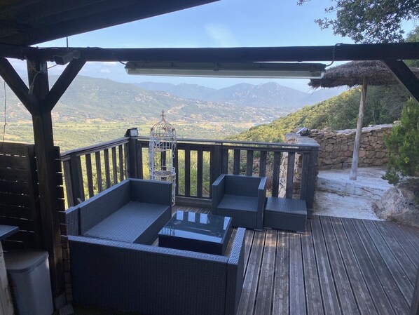 A wooden deck with wicker furniture and a birdcage, overlooking a mountainous landscape.