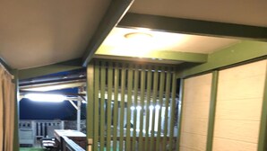 A narrow corridor with a wooden bench, a small table with a yellow object, and a green artificial turf leading to a deck area.