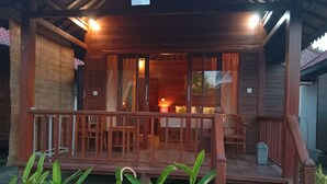A wooden cabin with a porch, a dining area, and a visible interior with a lit fireplace. - Svaha Nusa Guest House (Lembongan Island)
