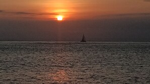 A sunset over a calm sea with a sailboat in the distance. - Svaha Nusa Guest House (Lembongan Island)