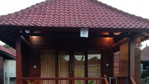 A wooden house with a tiled roof, a porch with a railing, and a small garden with young plants. - Svaha Nusa Guest House (Lembongan Island)