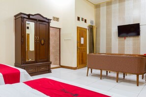 A hotel room with a wooden wardrobe, a television mounted on the wall, a sofa, and two beds with red and white bedding. - RedDoorz @ Pataruman Garut (Garut)