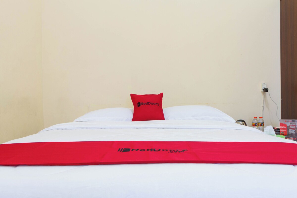 A bed with a white and red bedspread, a red pillow, and a white pillow.