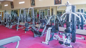 Ein Fitnessraum mit verschiedenen Trainingsgeräten, einem roten Teppichboden und Spiegeln an den Wänden.