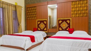 Ein Hotelzimmer mit zwei Betten, jeweils mit weißer Bettwäsche und roten Akzenten. Das Zimmer verfügt über hölzerne Kopfteile mit Verzierelementen und einen großen Spiegel über den Betten.