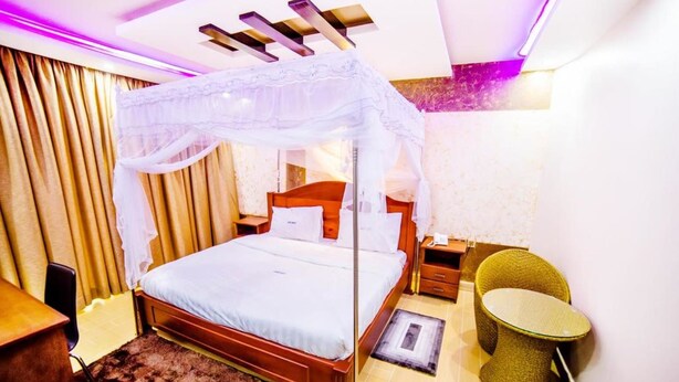 Habitación de hotel con cama con dosel, una pequeña mesa redonda, una silla y una mesita de noche con lámpara.
