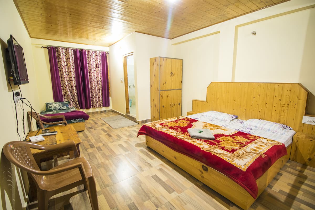 A bedroom with a wooden bed, a wooden wardrobe, a wooden desk, and a chair.