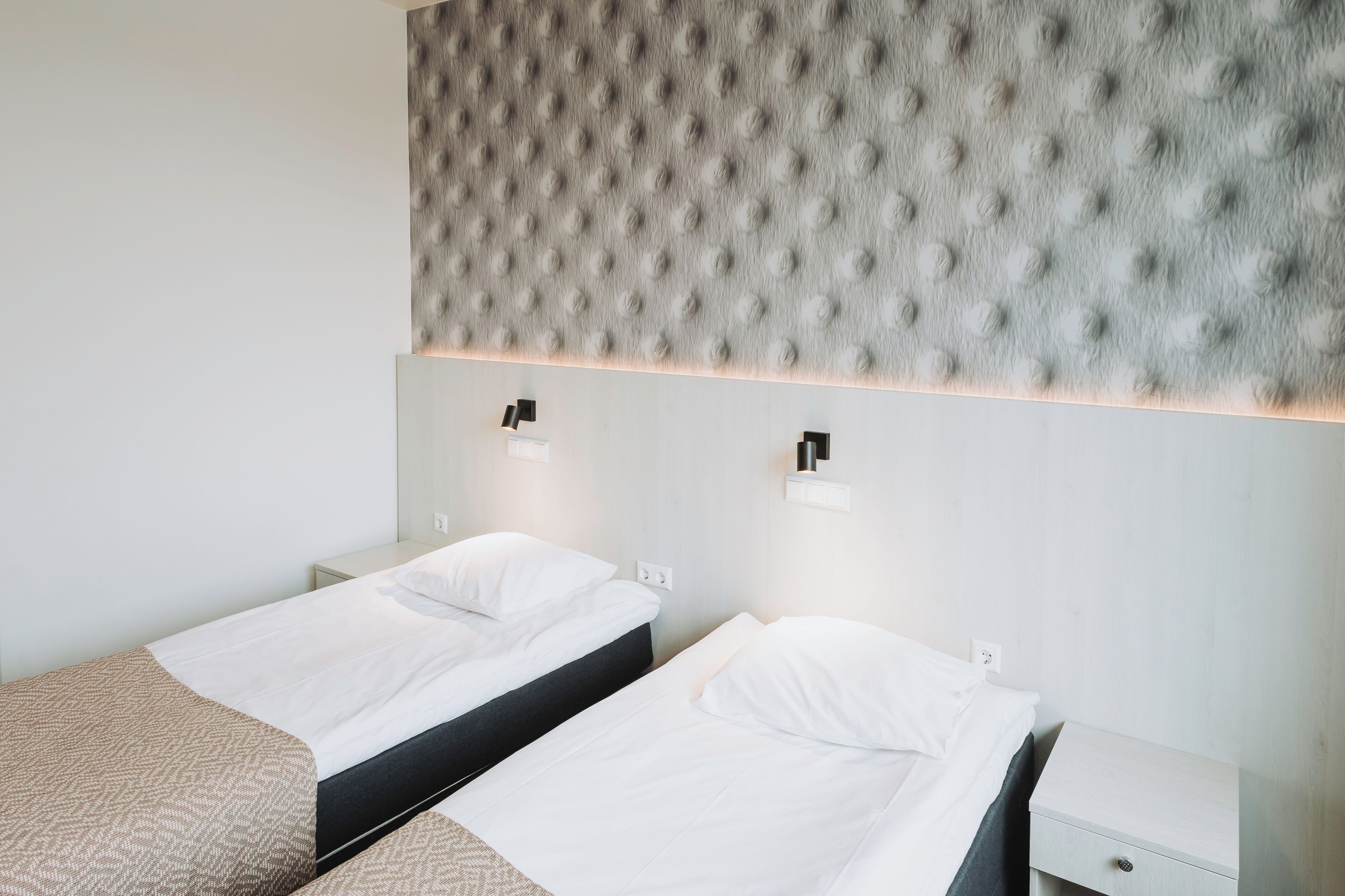 Une chambre d’hôtel avec deux lits simples, une tête de lit capitonnée, des lampes de chevet et une petite table de chevet avec un tiroir.