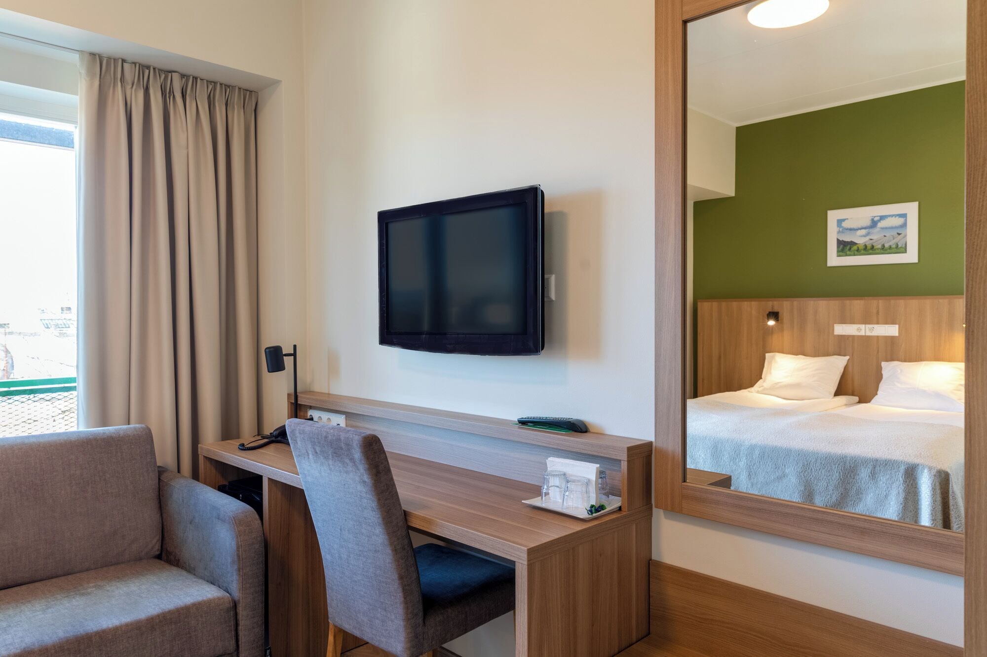 Habitación de hotel con cama, escritorio con silla, televisión y un espejo grande que refleja el espacio.