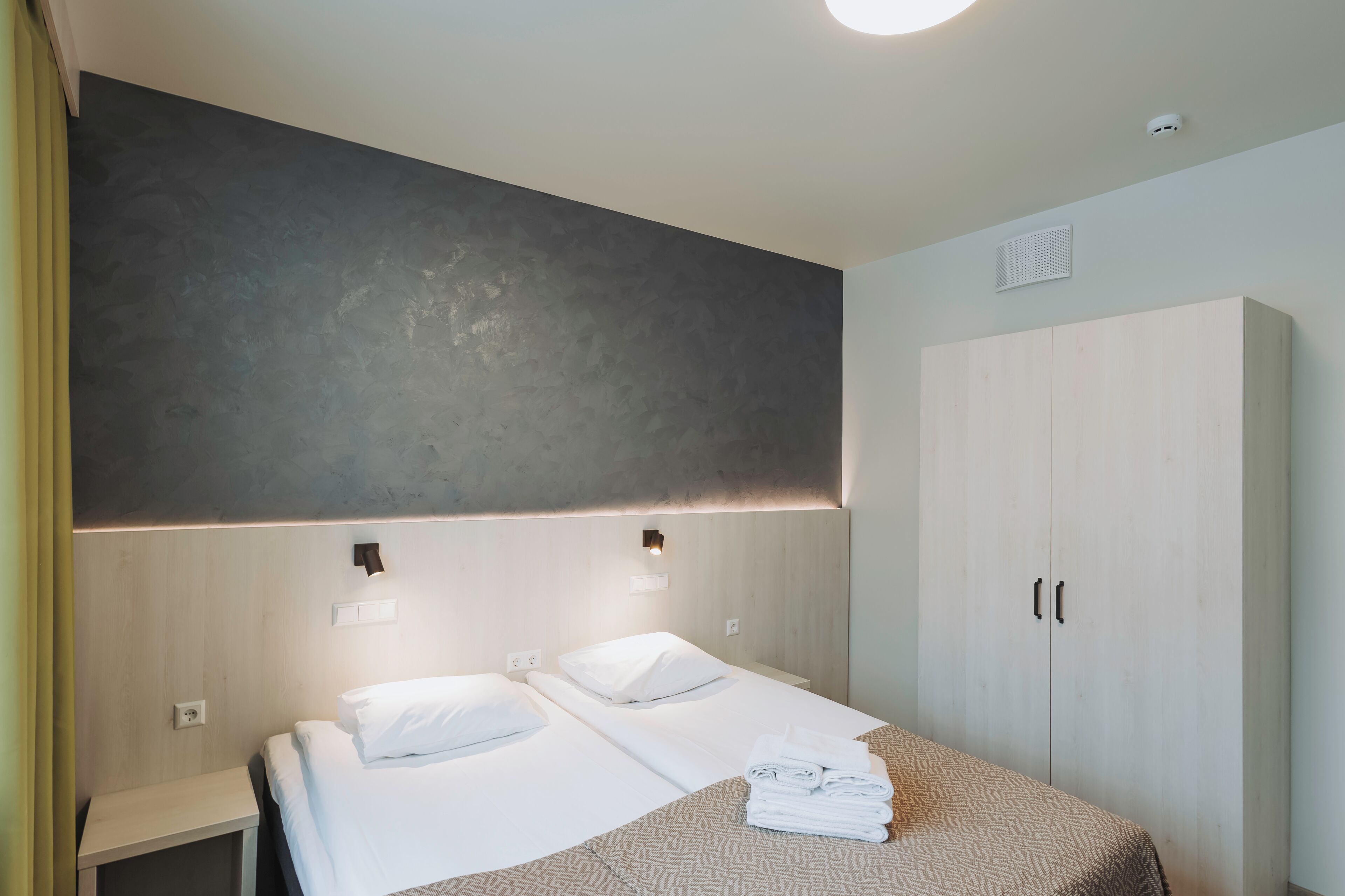 Een hotelkamer met twee bedden, een kledingkast en een wandlamp.