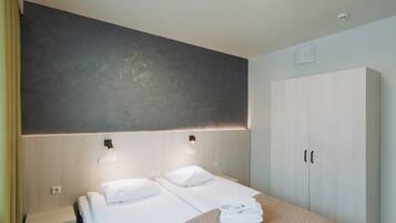 Habitación de hotel con dos camas, un armario y una lámpara fijada a la pared.