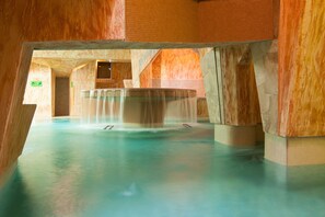 Una piscina interior amplia con múltiples fuentes y un diseño de pared de piedra.