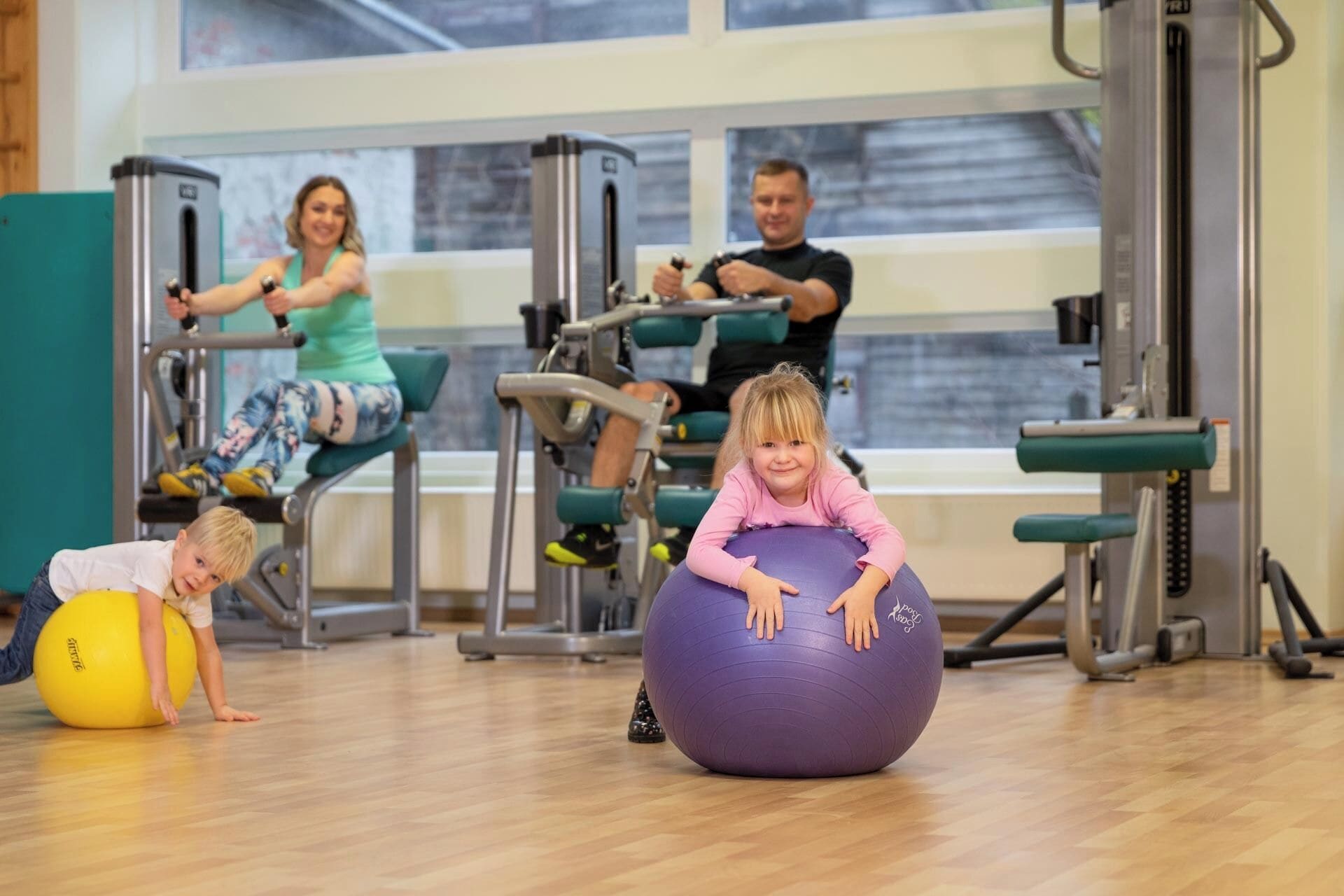 Een sportschool met trainingsapparatuur, een houten vloer en grote ramen.