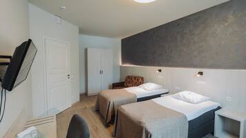 A modern hotel room with two single beds, a desk, a chair, a wardrobe, and a television.