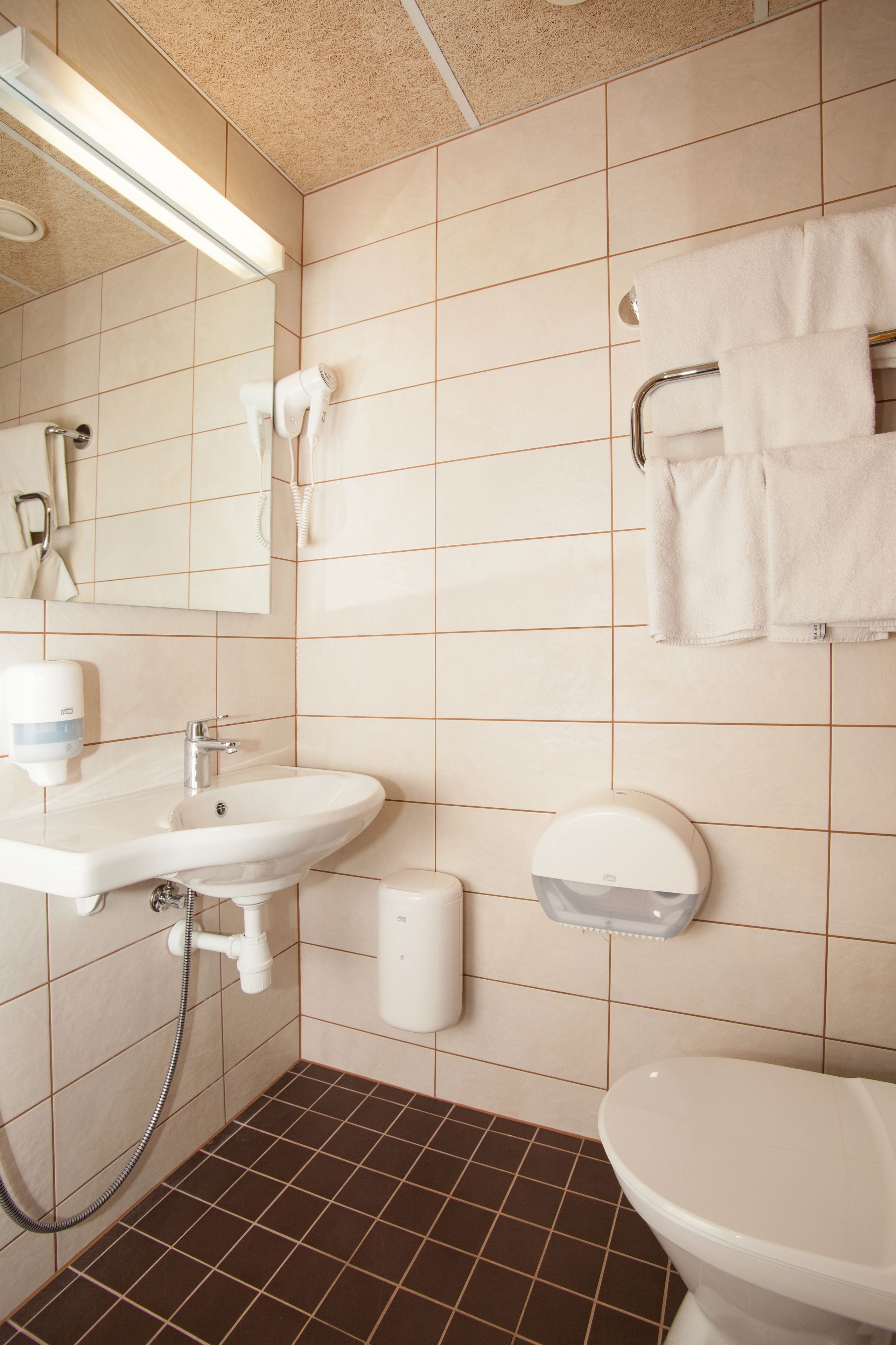 Un baño con lavamanos, espejo, toallero y retrete.