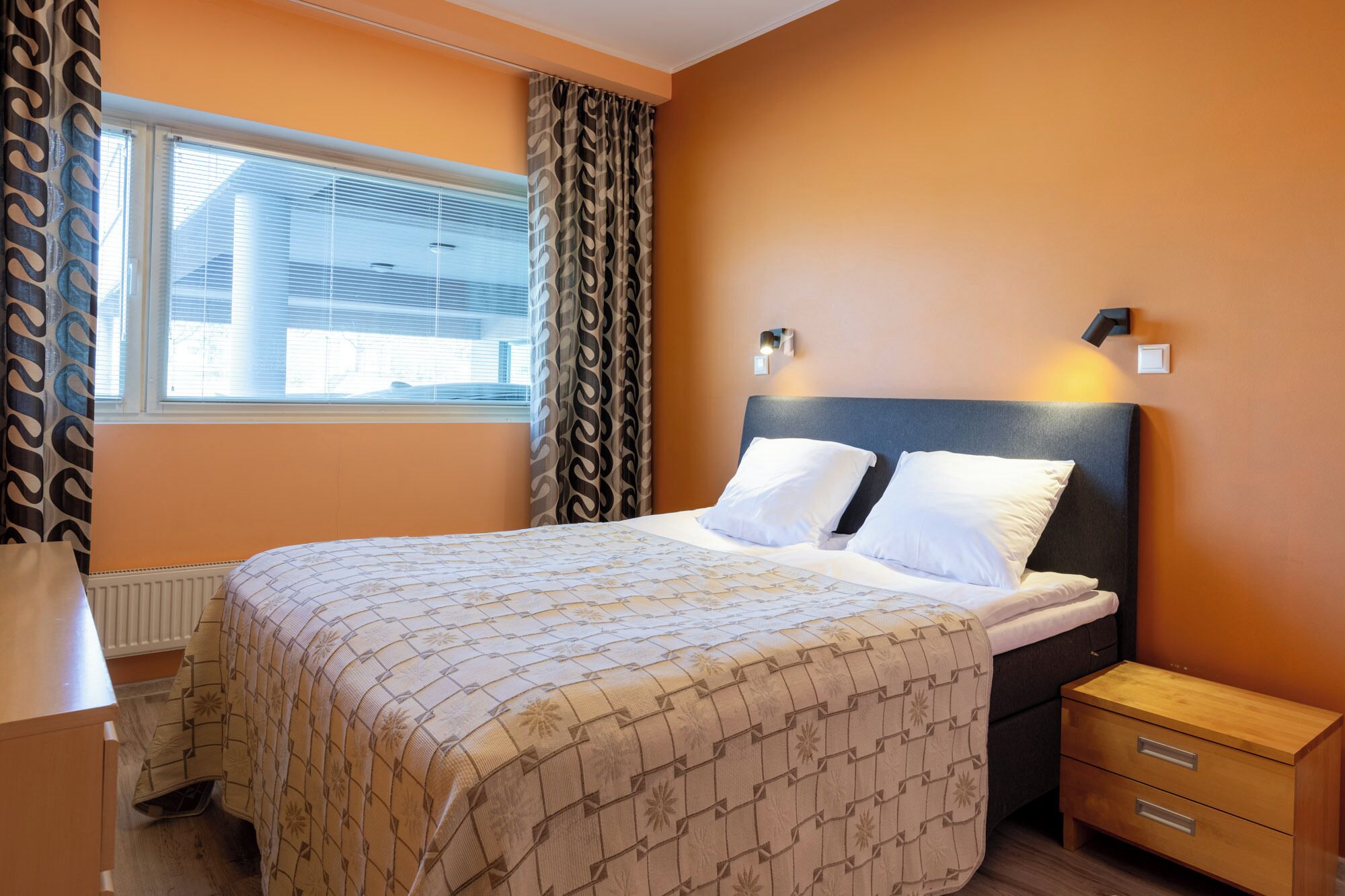Une chambre d’hôtel avec un lit, une table de chevet, une lampe et une fenêtre avec des rideaux.