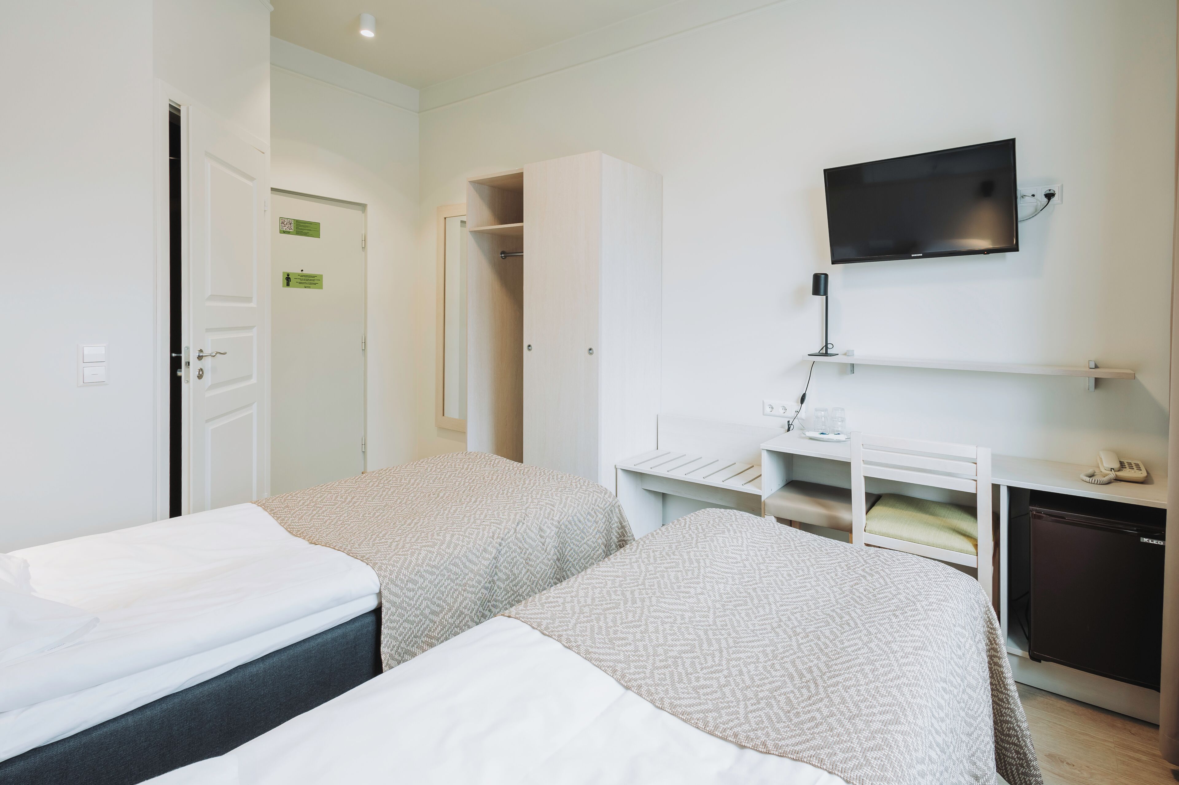 Ett hotellrum med två sängar, en TV, ett skrivbord och ett litet kylskåp.
