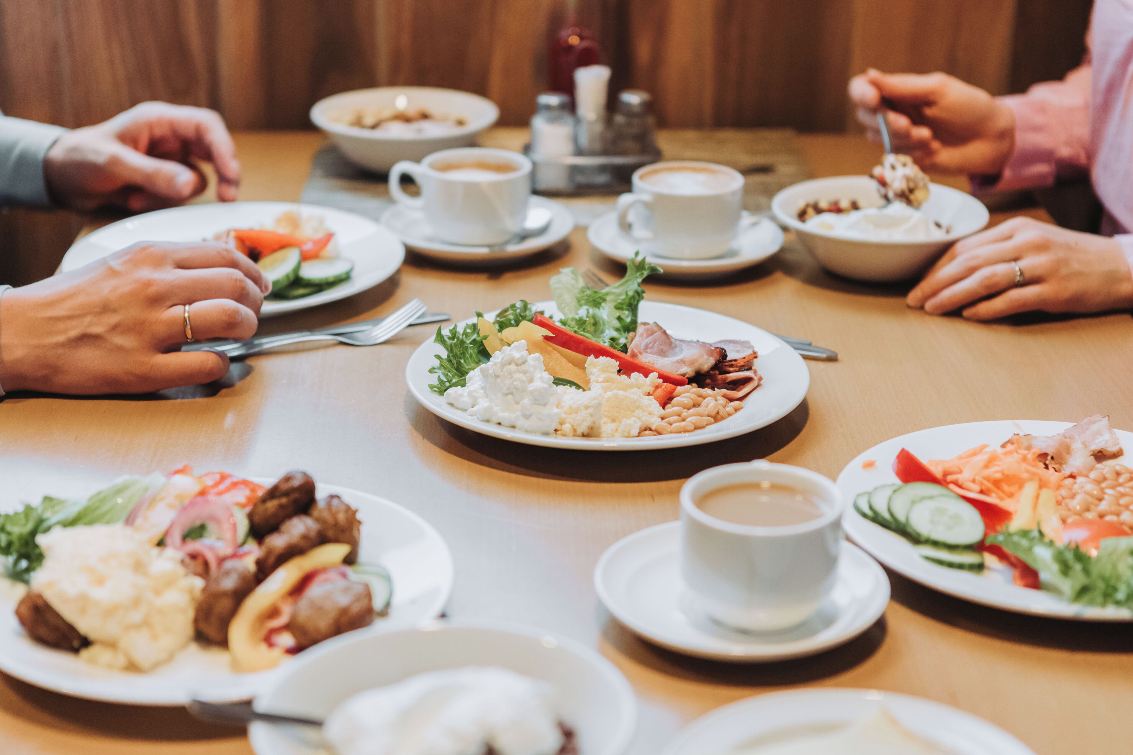 Ein Esstisch mit verschiedenen Speisen, Kaffeetassen und Personen beim Essen.