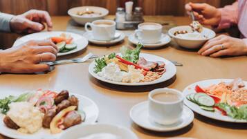 Ein Esstisch mit verschiedenen Speisen, Kaffeetassen und Personen beim Essen.
