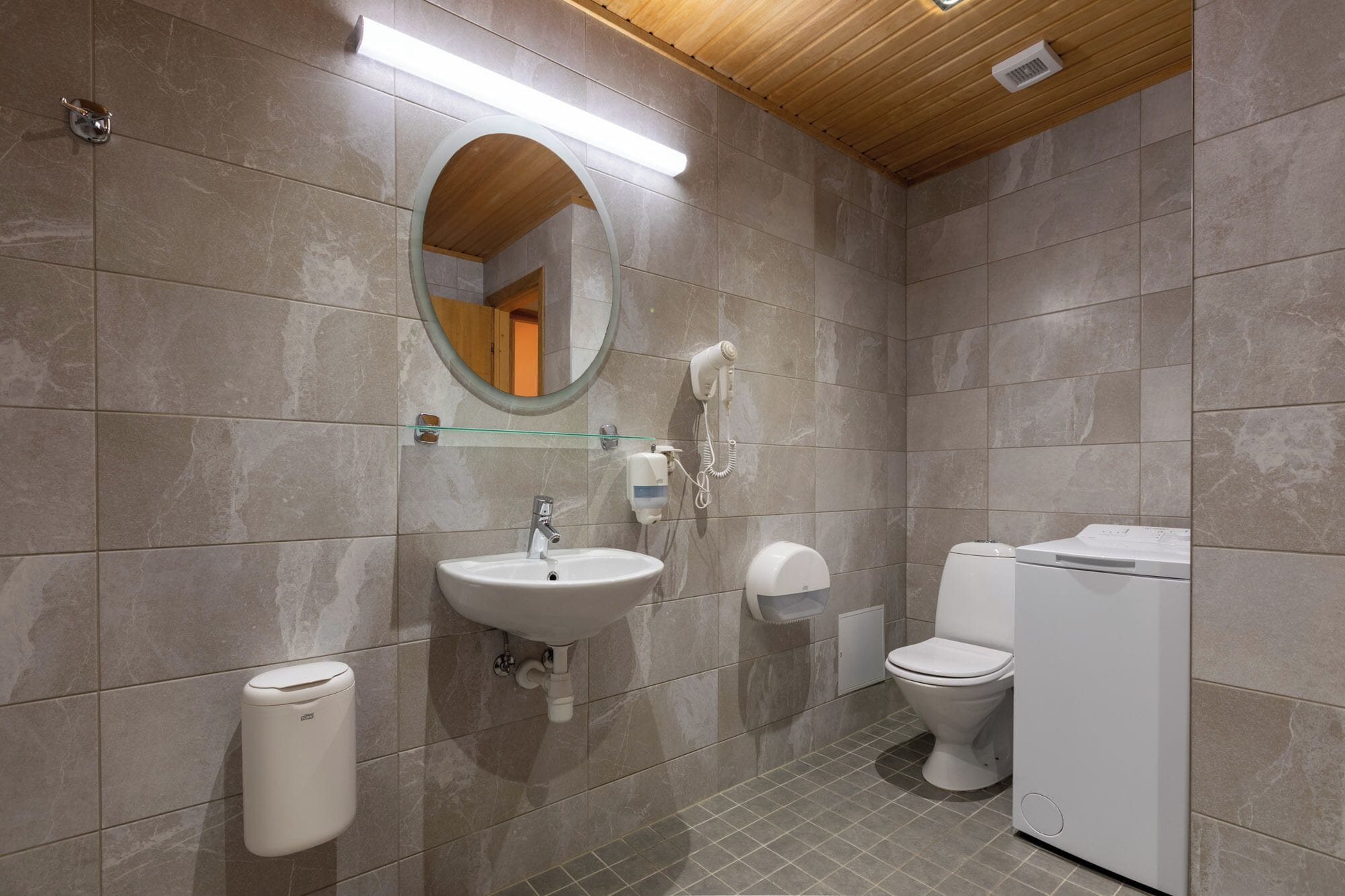 Un baño con lavamanos, espejo, inodoro y lavadora.