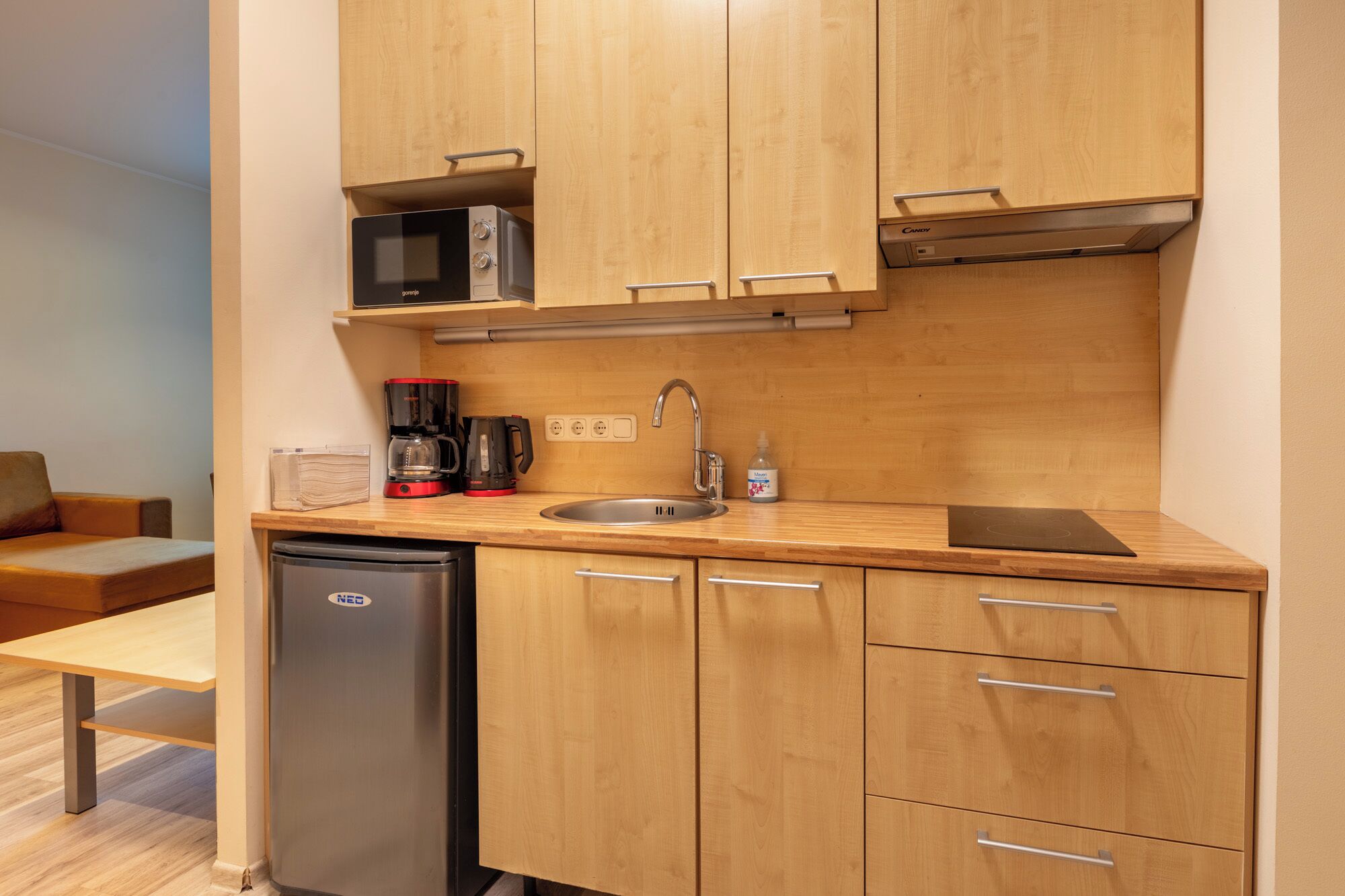 Eine kleine Küche mit Holzausstattung, einer integrierten Mikrowelle, einer Kaffeemaschine, einem Spülbecken und einem Kühlschrank.