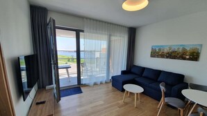 A modern living room with a sofa, a TV, a dining table, and a balcony with a view of the water. - Viiking Spa Hotel (Parnu)