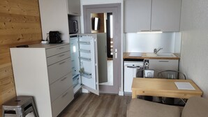 A compact kitchen with a refrigerator, microwave, and sink. There is a small dining area with a table and chairs.
