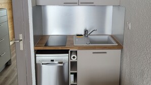 A compact kitchen with grey cabinets, a wooden countertop, a stainless steel sink, and a dishwasher.