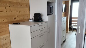 A compact kitchen with a microwave, coffee maker, and a small stool.