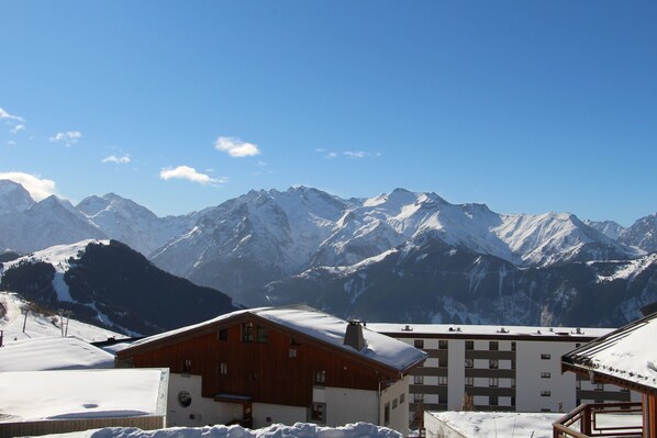 A mountain resort with snow-covered peaks and buildings with balconies. - Resort center with parking, south-facing terrace, not overlooked (Alpe d'Huez)