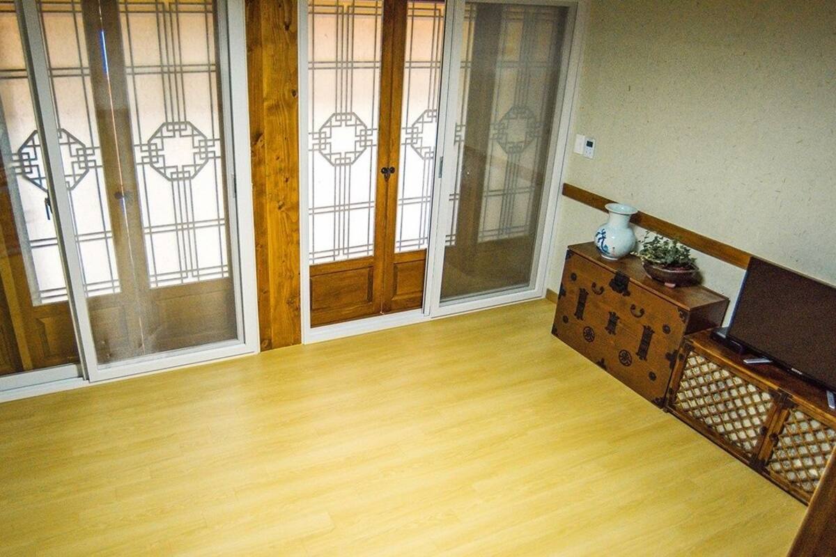 Una habitación con piso de madera, puertas correderas con diseños geométricos y un pequeño mueble de madera con un florero y una planta.