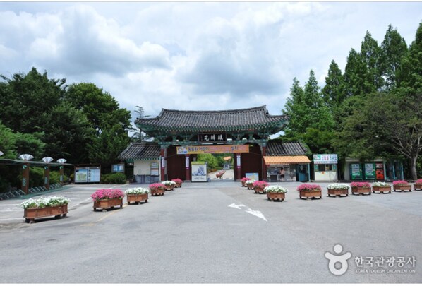 A traditional Korean gate with a sign, surrounded by potted flowers and trees. - Yewondang (Jeonju)