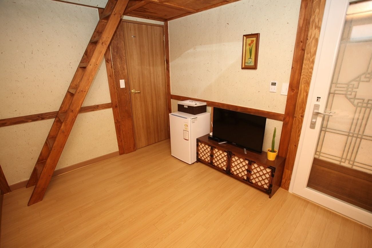 Ein Zimmer mit Holzboden, einem weißen Kühlschrank, einem Flachbildfernseher auf einem Holzständer und einer Tür mit Holzrahmen.