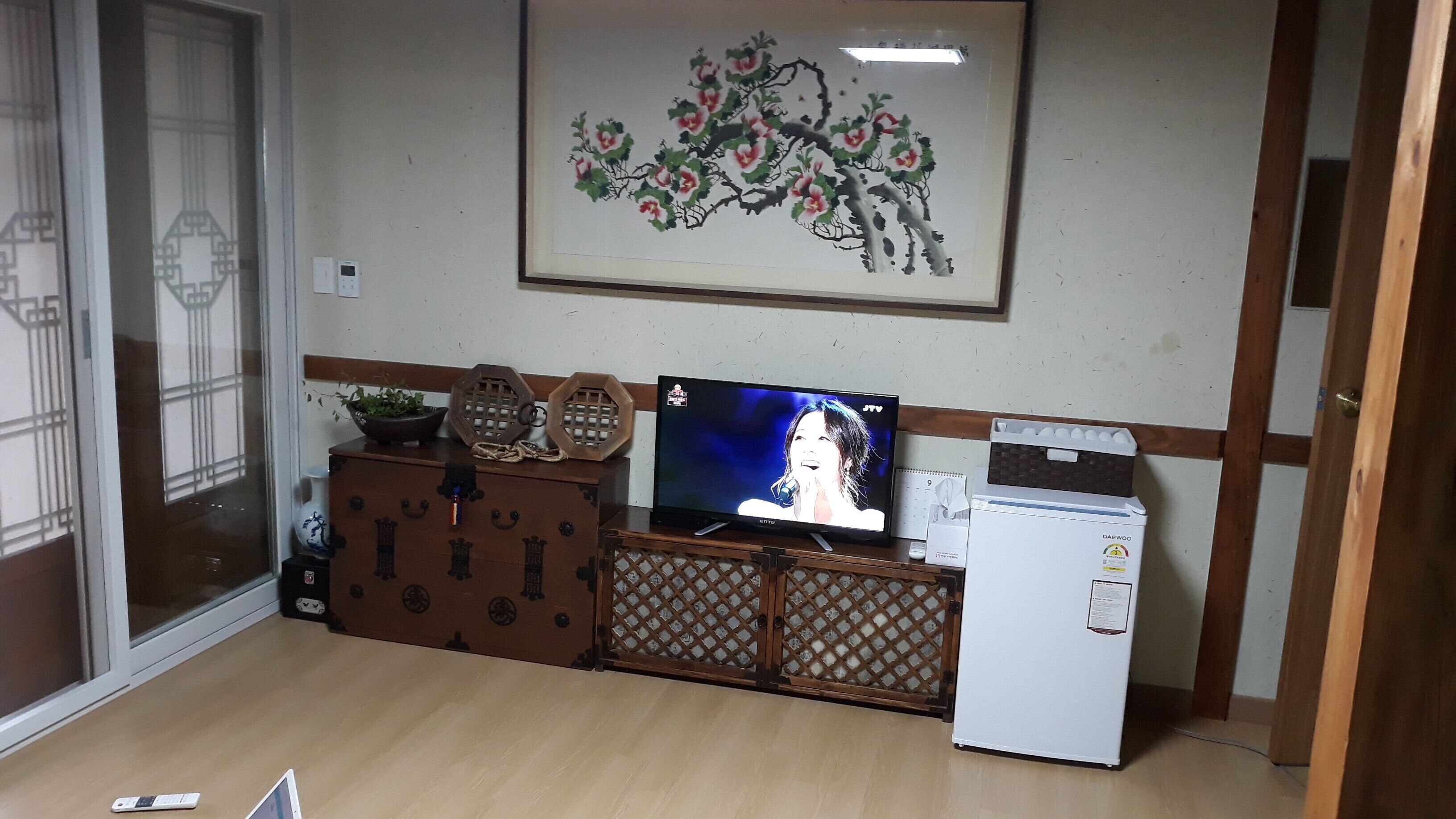 Una habitación con un armario de madera, un televisor, un refrigerador y un cuadro decorativo en la pared.