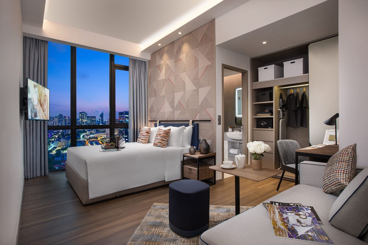 Una habitación de hotel moderna con una cama grande, un sofá, un escritorio y un vestidor.