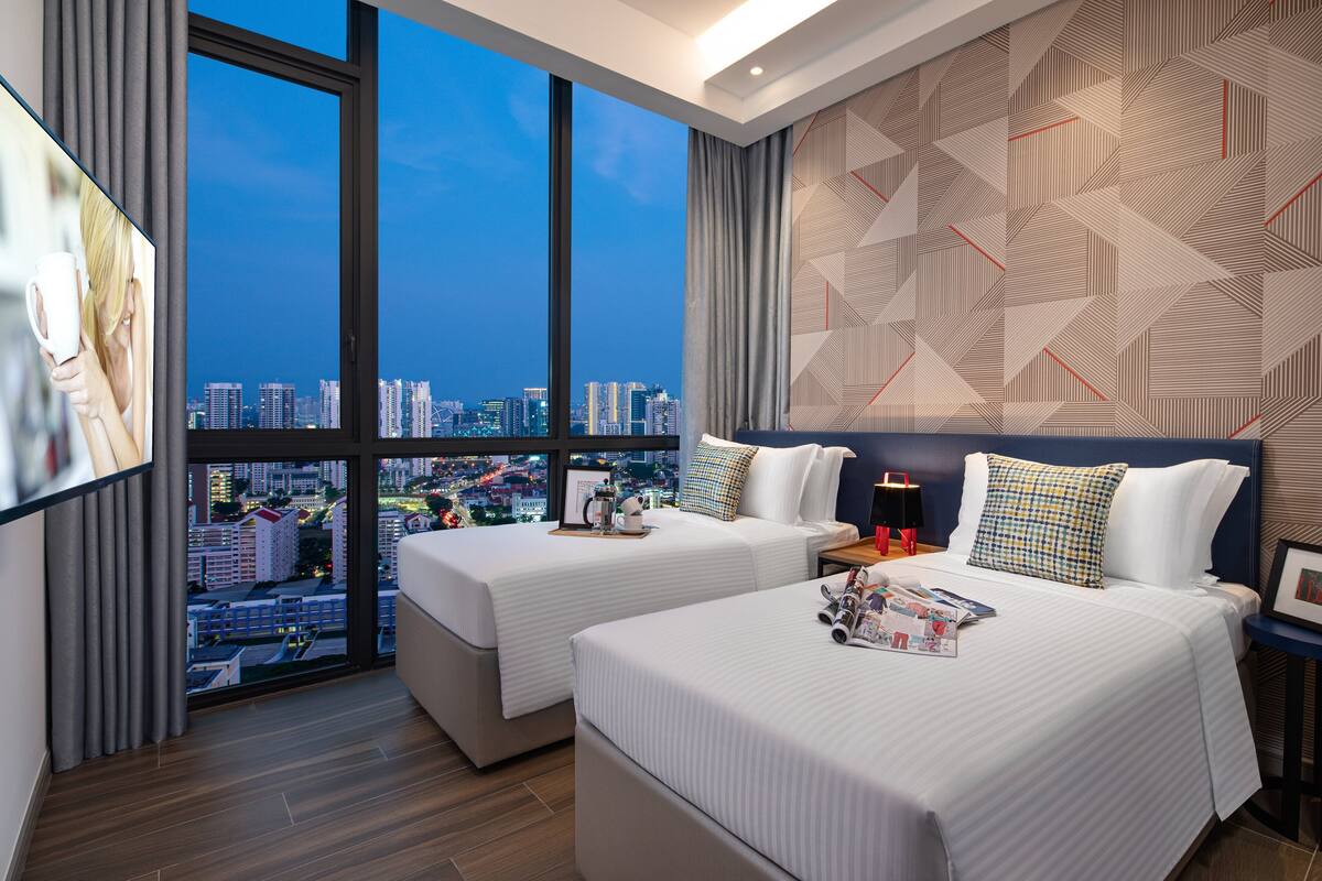 Habitación de hotel con dos camas, vista a la ciudad y un diseño geométrico en la pared.